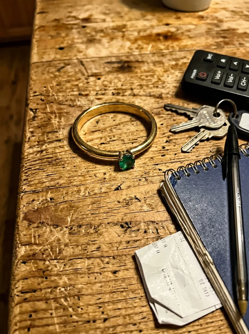 Тонкое золотое кольцо с изумрудом, снятое на телефон на деревянном столе