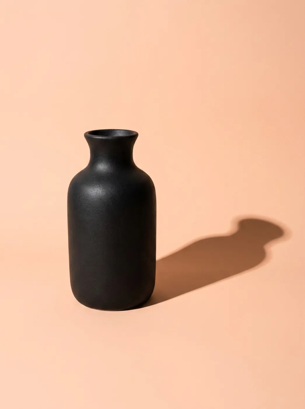 Матовая чёрная ваза на персиковом фоне с длинной графичной тенью